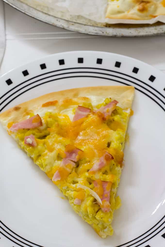 One slice of canadian bacon breakfast pizza on a black and white plate.