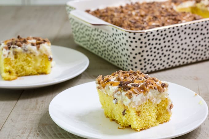 One piece of cake on a plate in the foreground and one piece of cake and the rest of it in the background.