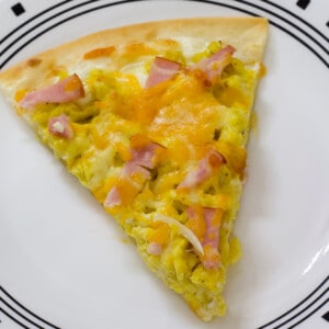 One piece of breakfast pizza on a white plate.