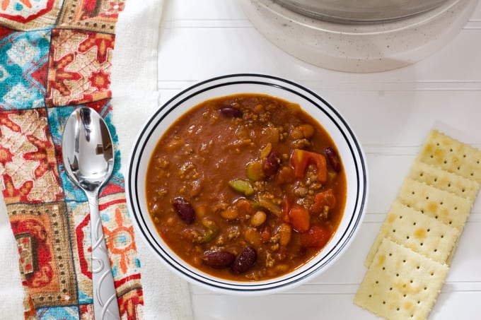 One bowl of chili with a spoon and crackers on the table beside it.