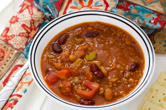 Close up view of a white bowl filled with chili and crackers beside it.