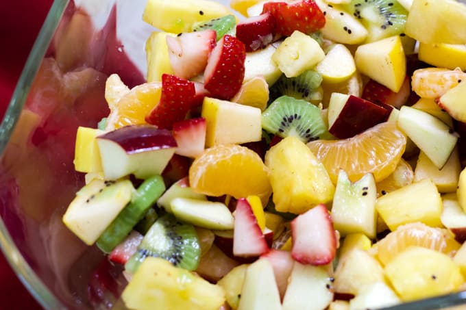 Chopped strawberries, apples, kiwi, pineapple and mandarin oranges in a large glass bowl.