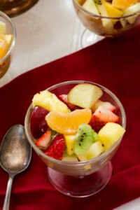 A small glass bowl of fruit and a tarnished silver spoon sitting on a maroon cloth napkin.