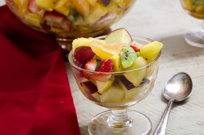 A small glass of fruit in the foreground and a large glass bowl of fruit in the background.