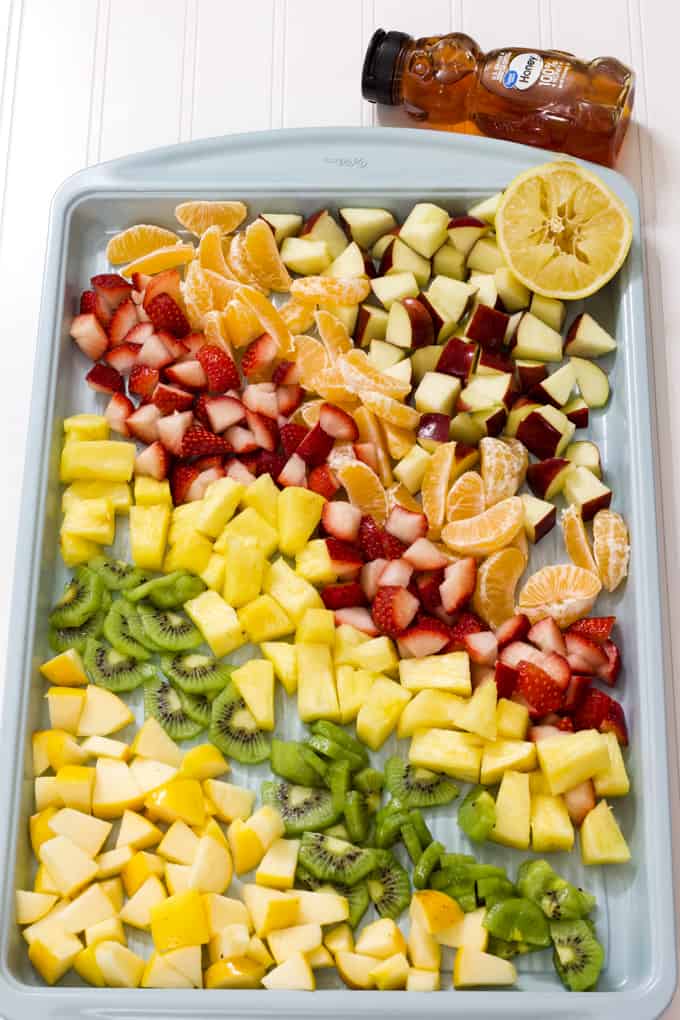A light blue sheet pan with chopped apples, kiwi, pineapples, and oranges on it.