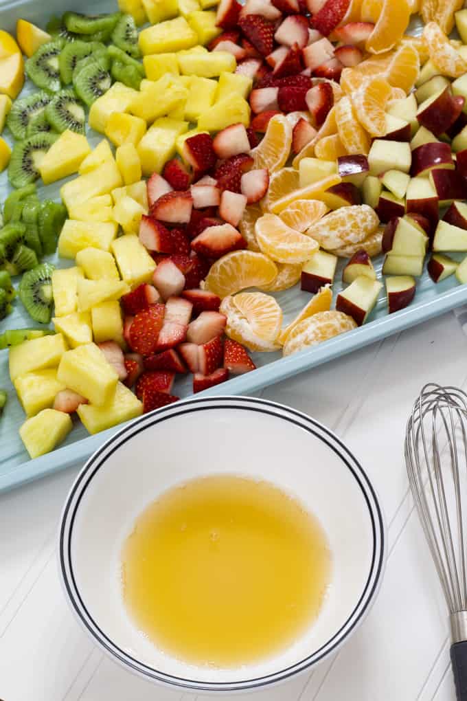 A small white bowl with honey lemon dressing in it with a pan of fruit in the background.