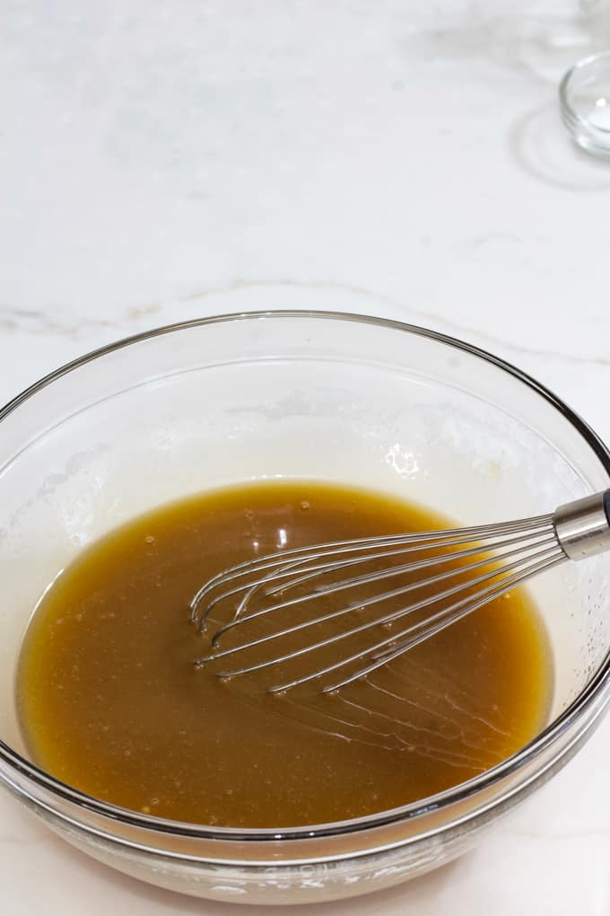The completed caramel sauce in a glass bowl with a wire whisk in it.