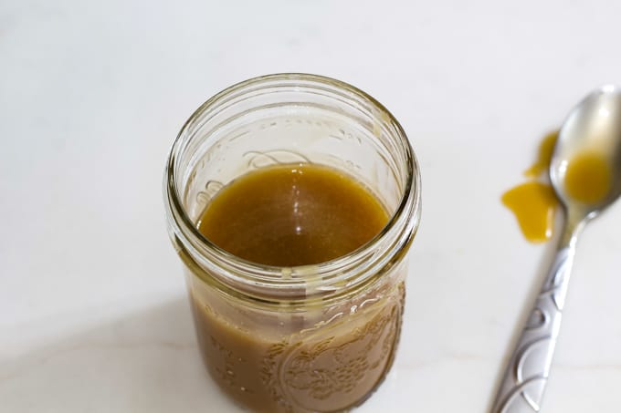 Overhead view of caramel sauce in a mason jar with a spoon on the table next to it.