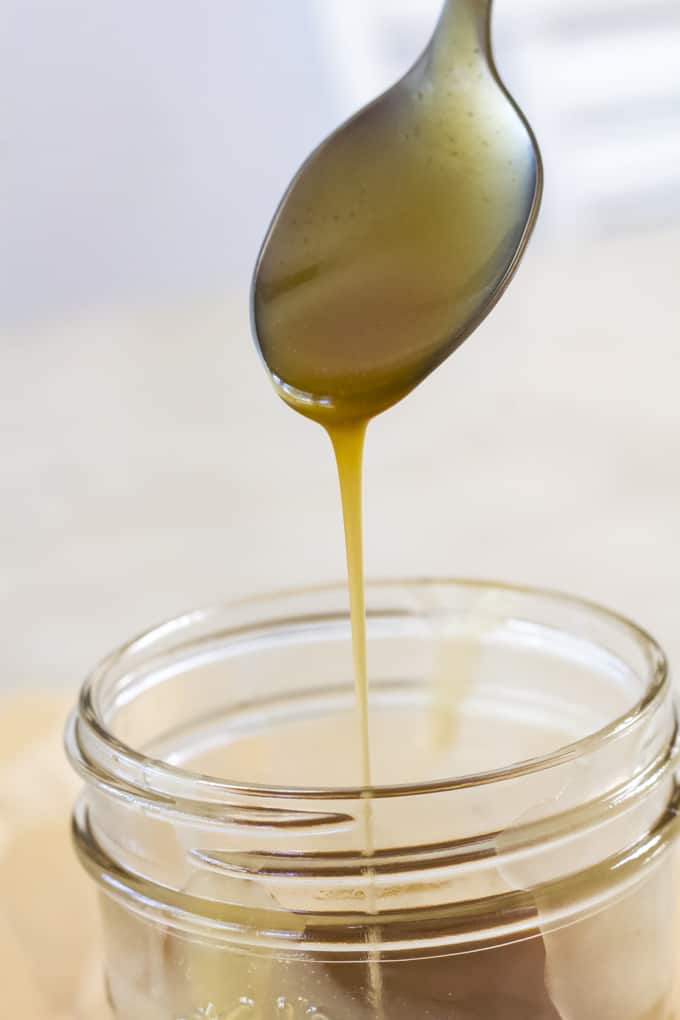 A spoon with a stream of caramel sauce going into a mason jar.