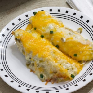 Close up view of two chicken enchiladas on a white and black plate.