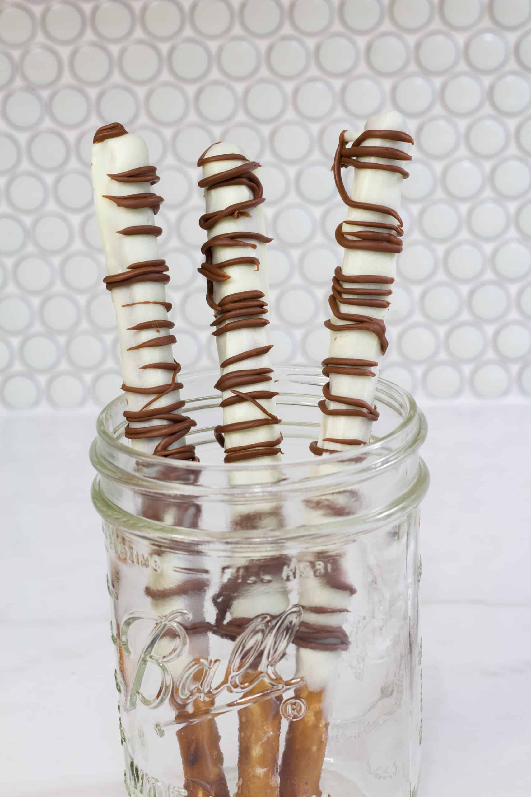 Three pretzel rods that have been dipped in white chocolate and have milk chocolate drizzled over them.