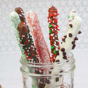 Several chocolate covered pretzel rods sticking up out of a glass jar.