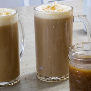 Two cups of caramel coffee with a small jar of caramel sauce in the foreground.