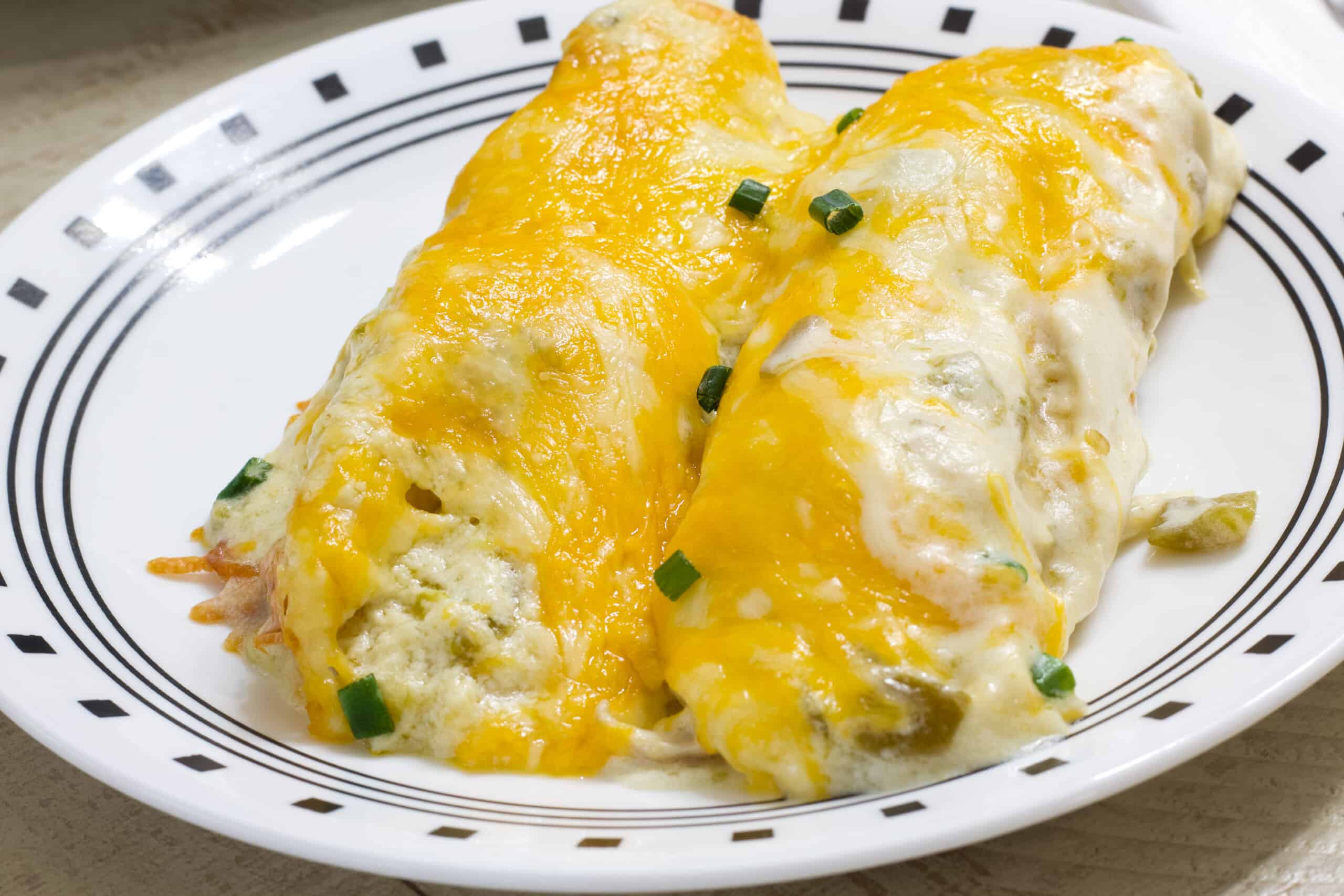Close up side view of two chicken enchiladas on a plate.