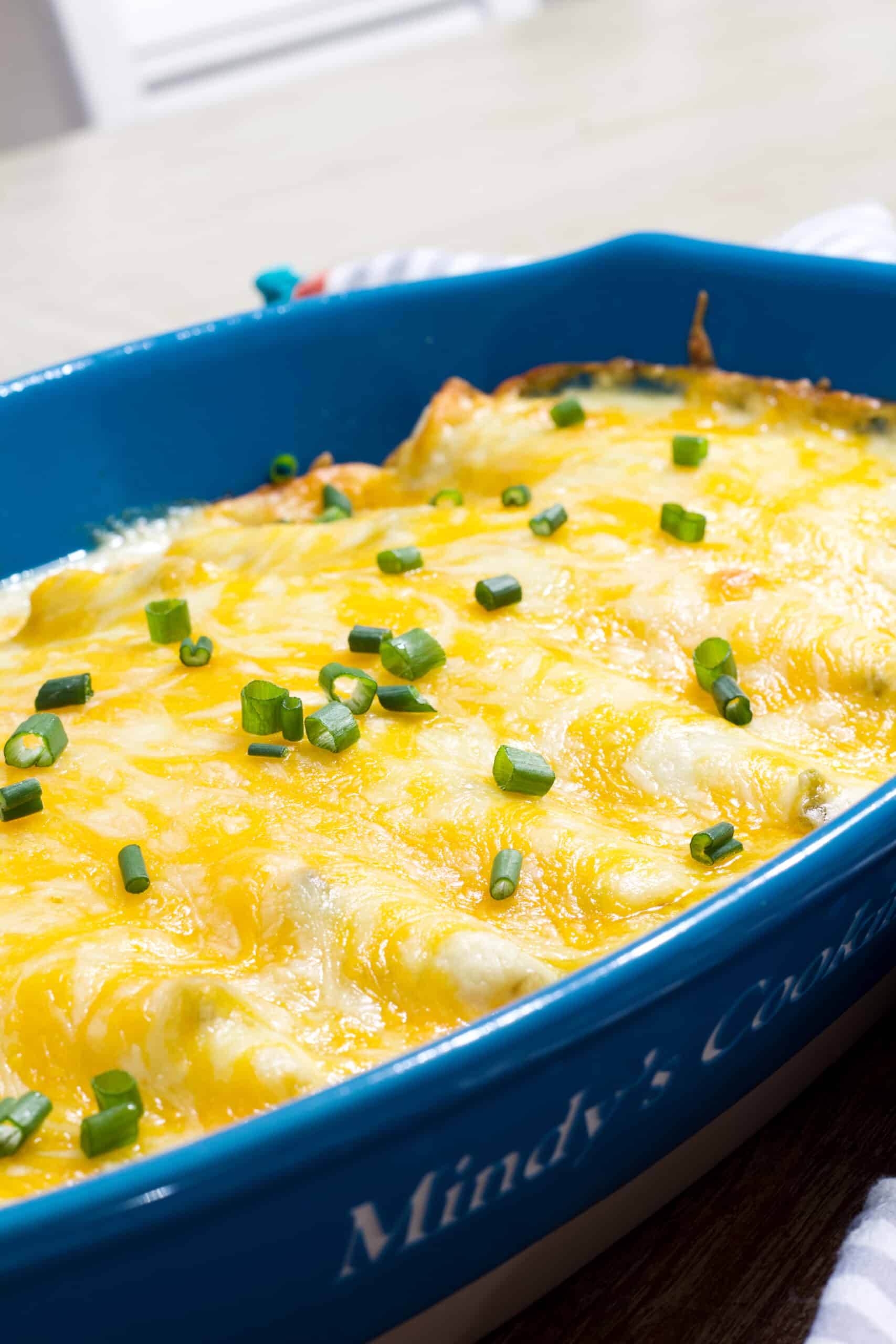 Side view of a blue casserole dish with all eight chicken enchiladas in it.