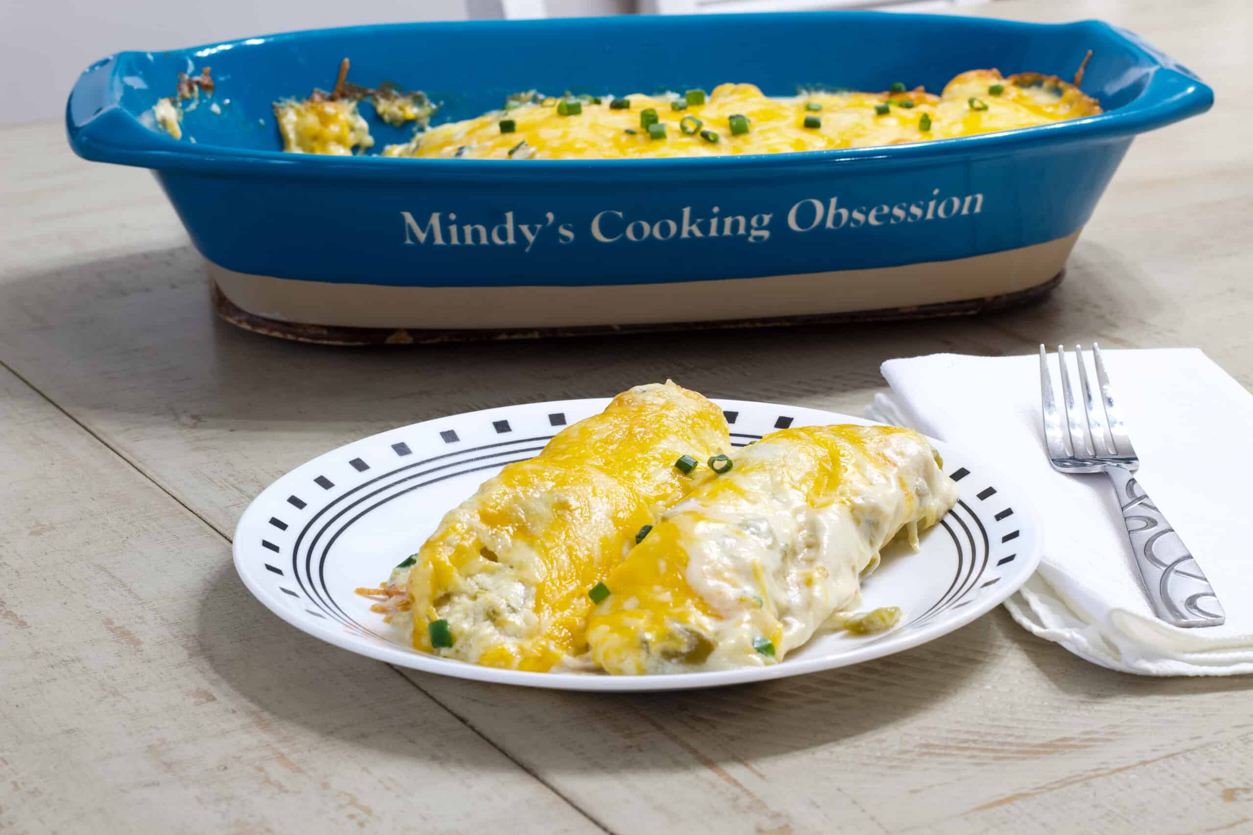 A plate of enchiladas in the foreground and the remaining enchiladas in a casserole dish in the background.