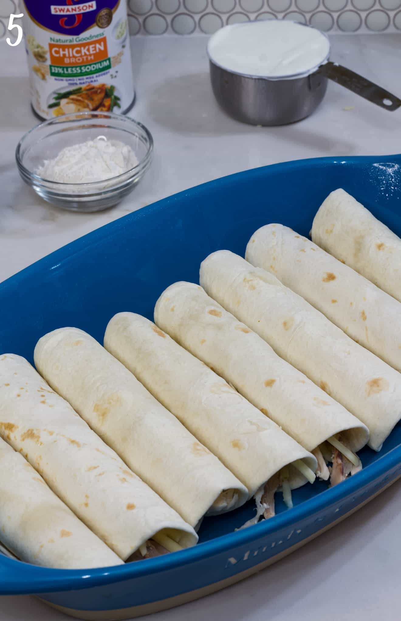 The enchiladas in a blue casserole dish ready to be topped with the cream sauce.