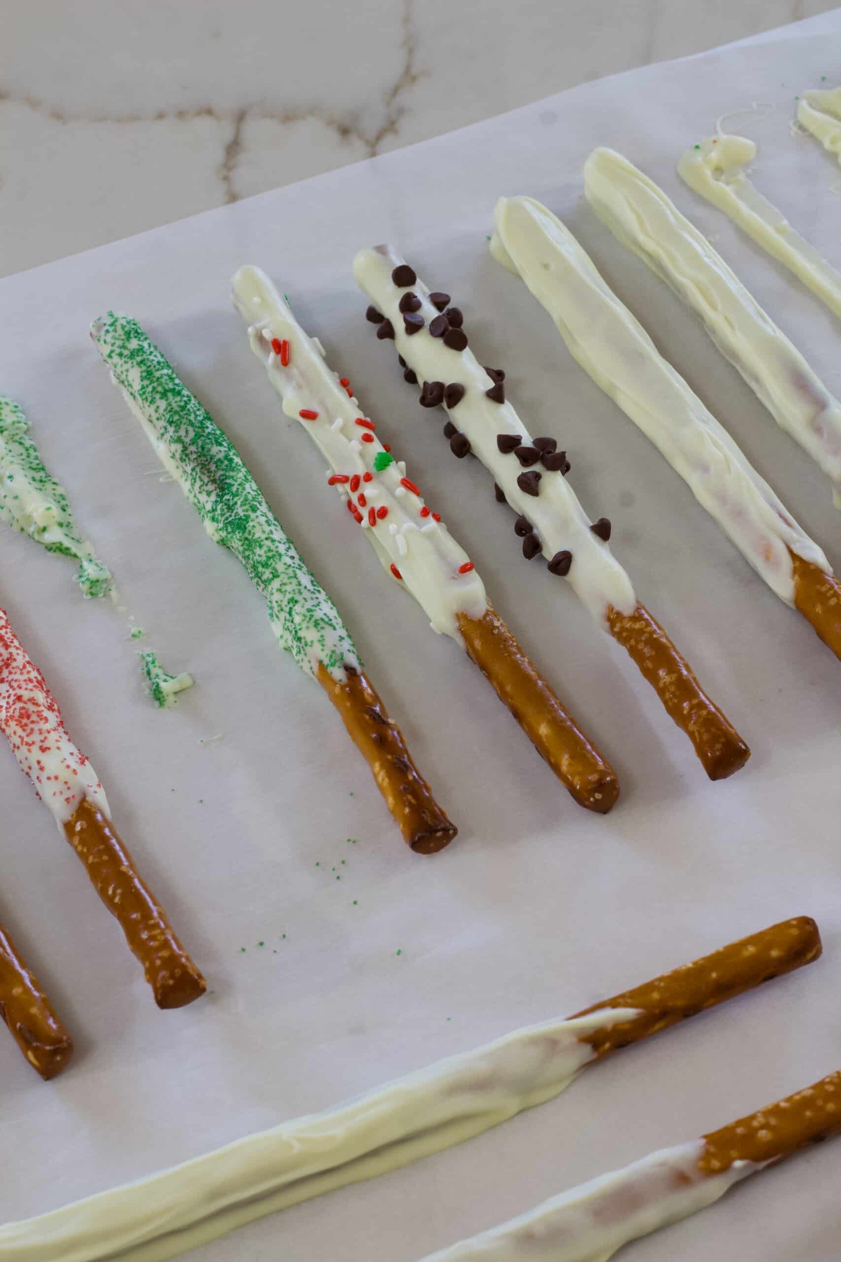 Many pretzel rods that have been dipped in white chocolate that are drying.