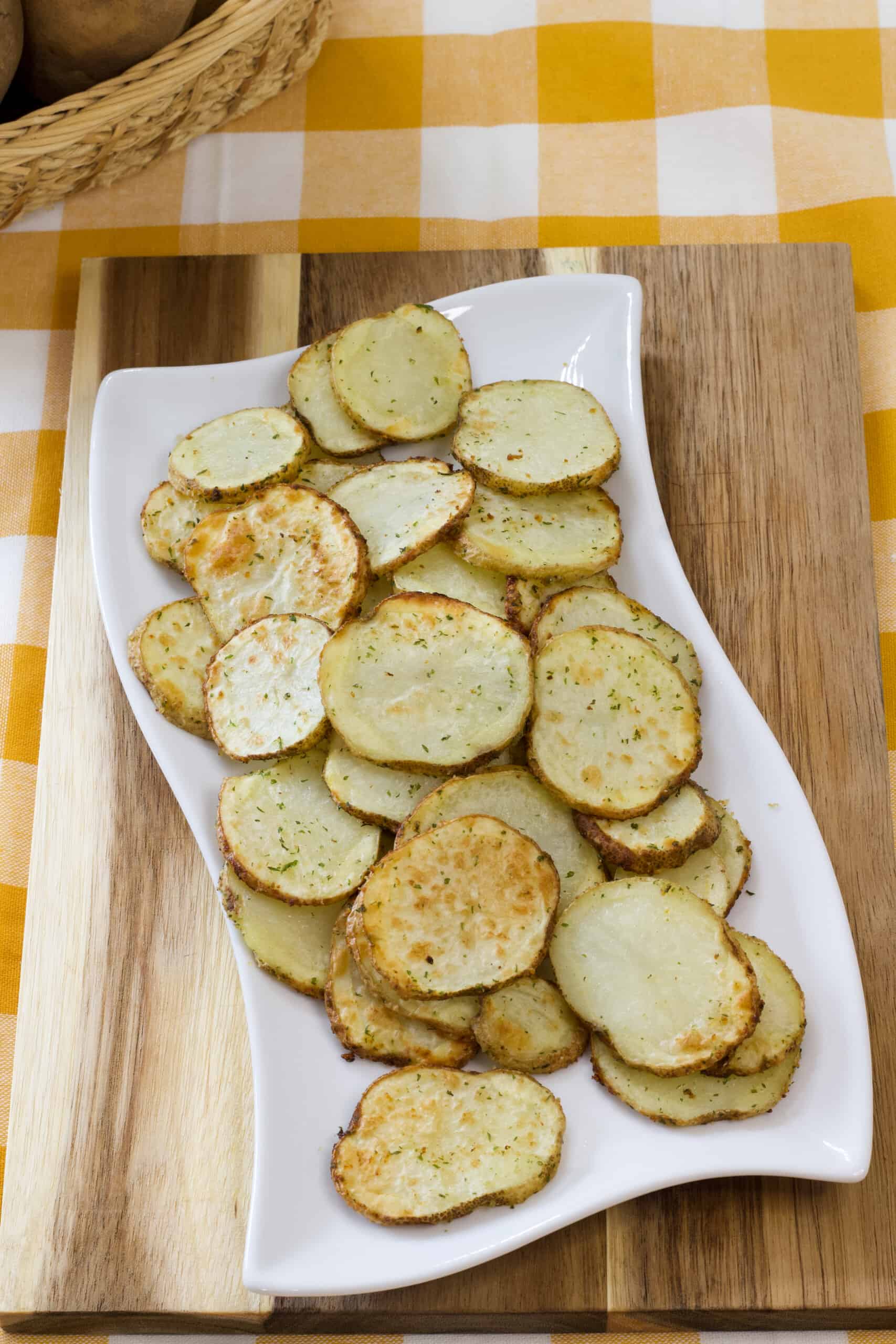 Vertical shot of the potatoes on a white plate on top of a cutting board and tea towel.