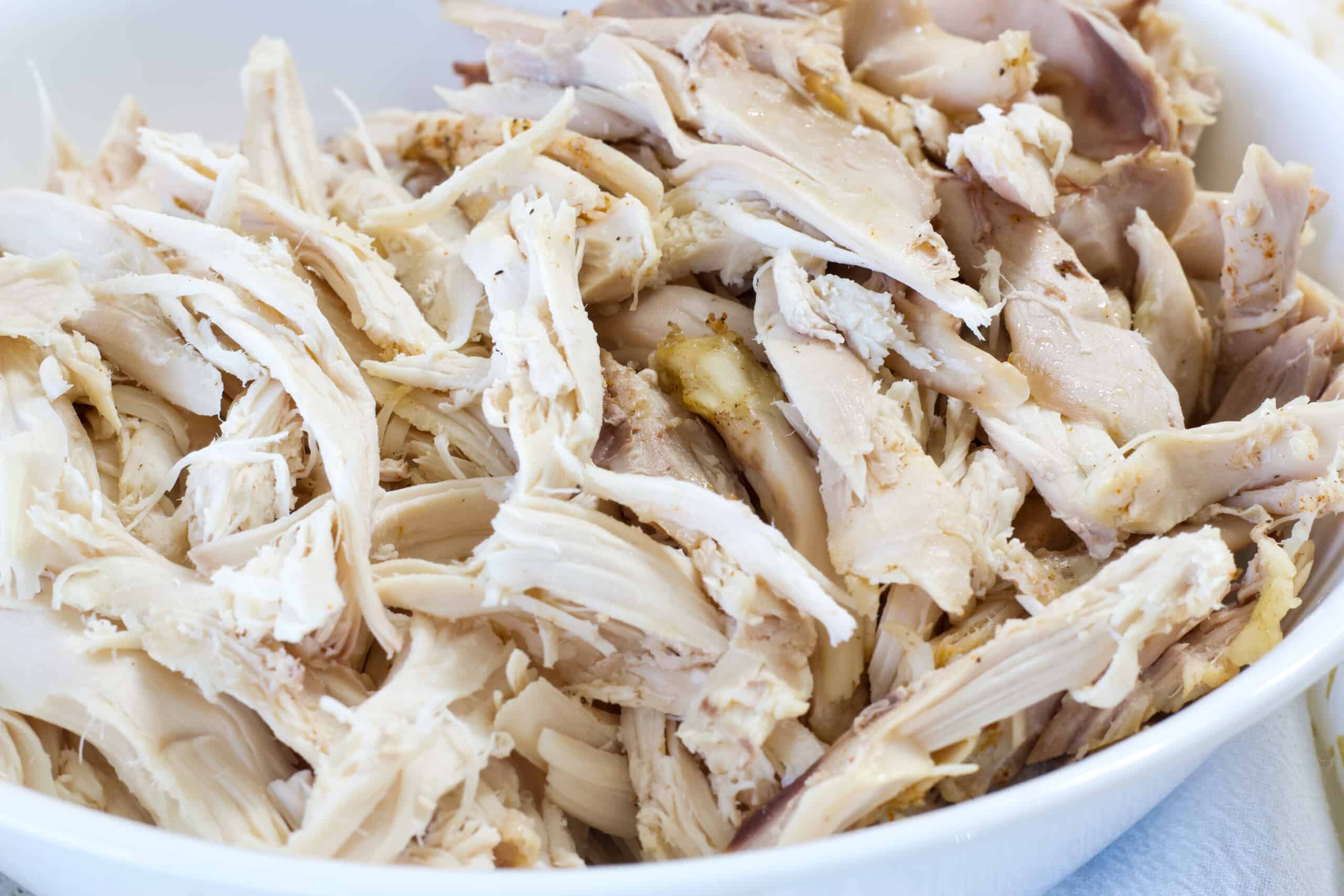 Close up of the shredded rotisserie style chicken in a white bowl.