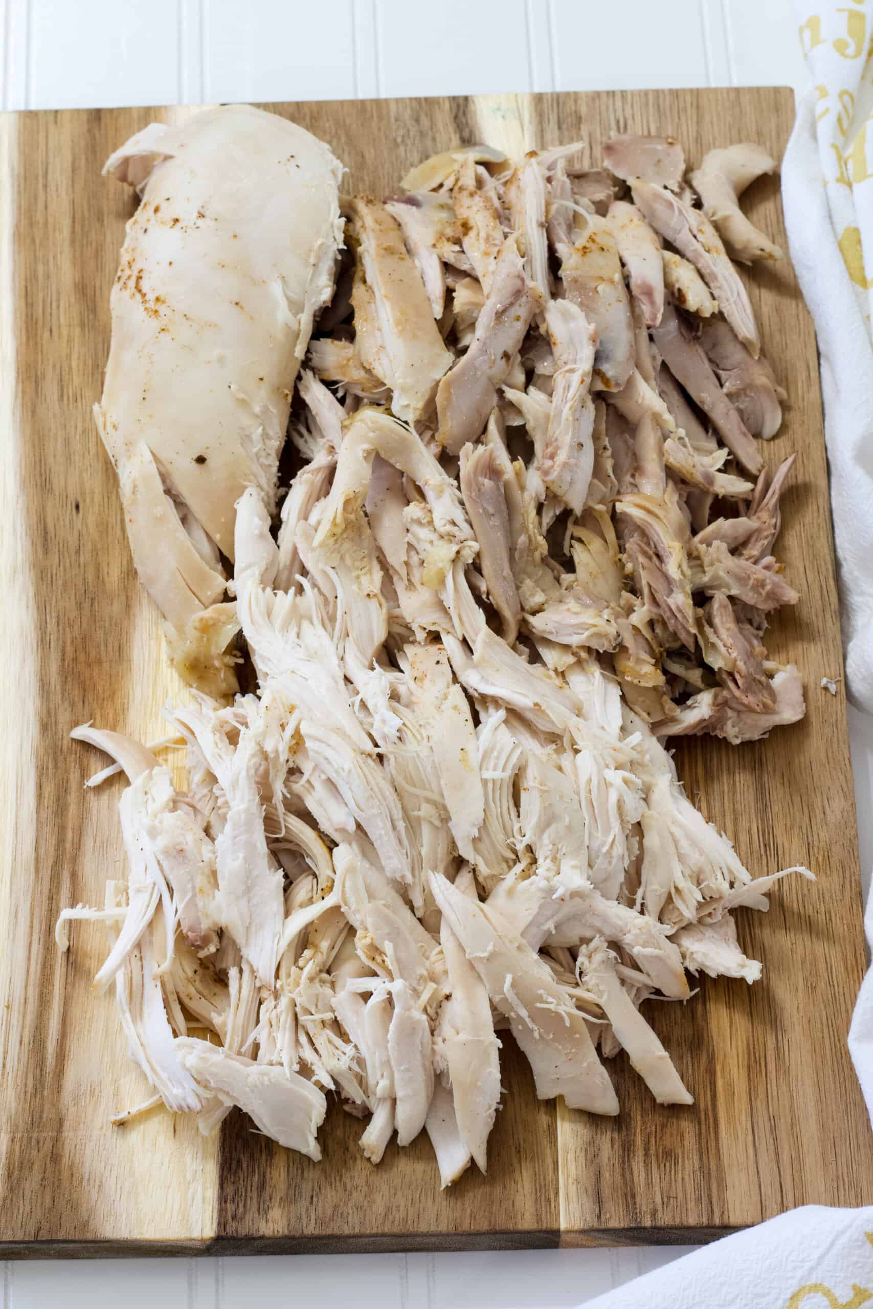 Vertical shot of shredded white and brown meat chicken on a wooden cutting board.