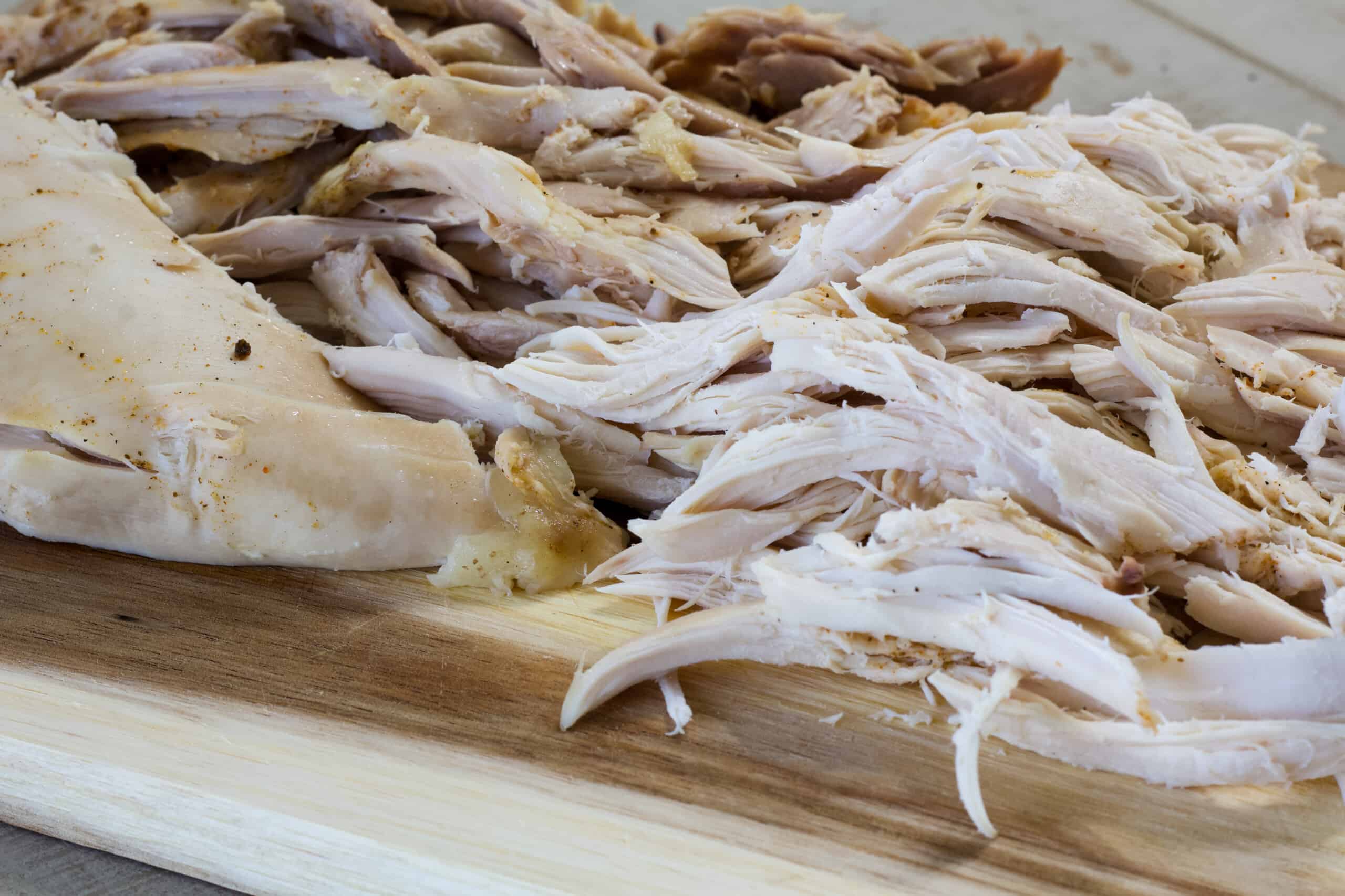 Close up side view of shredded chicken on a wooden cutting board.
