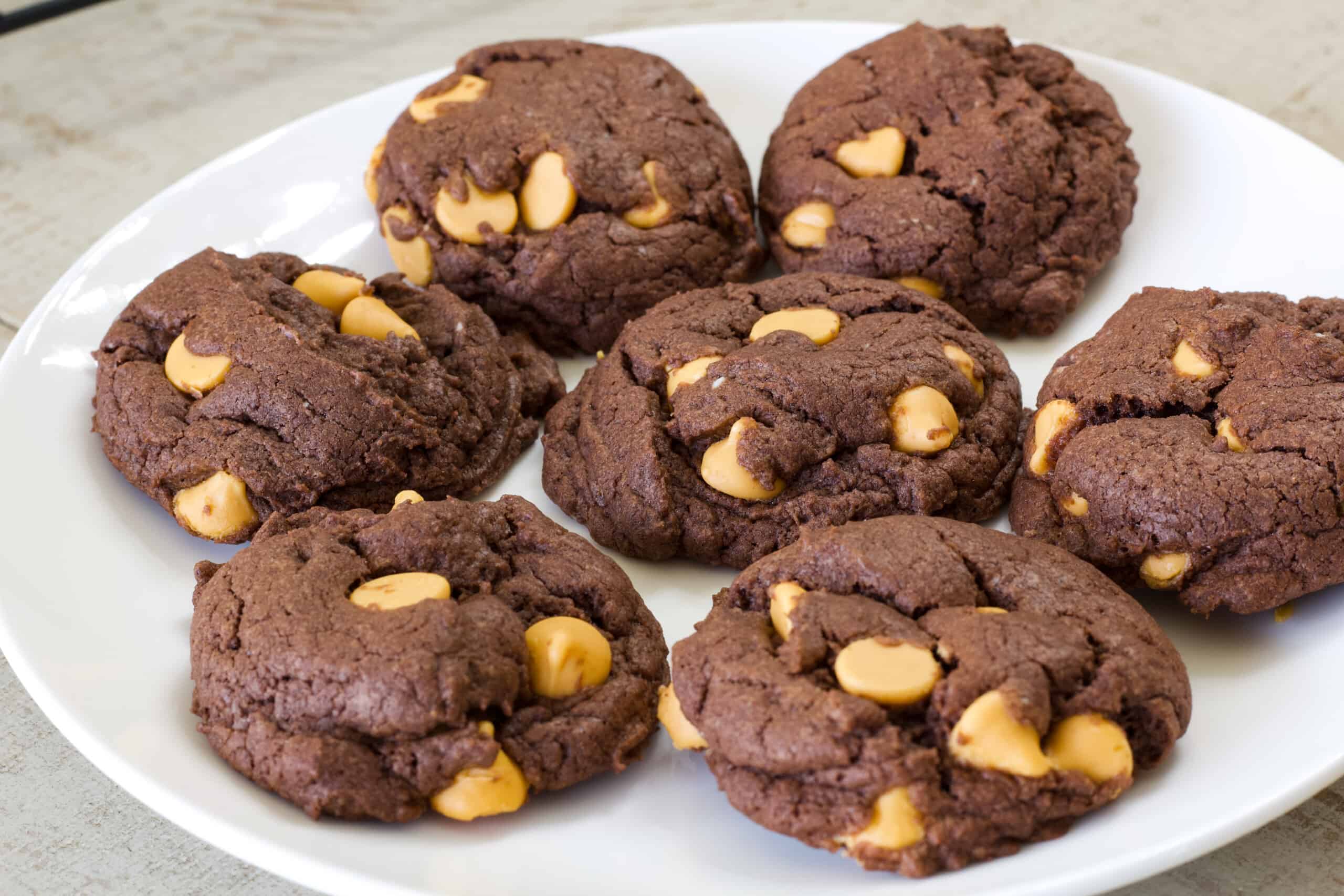 A white plate with seven chocolate butterscotch chip cookies on it.