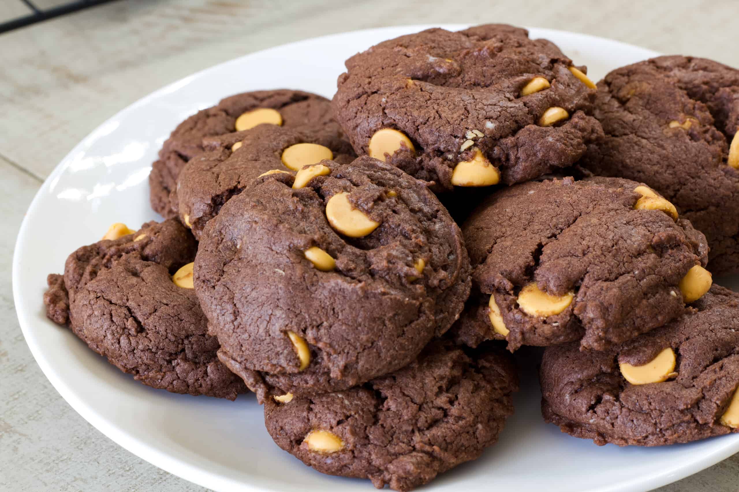 A white plate with many chocolate butterscotch chip cookies on it.