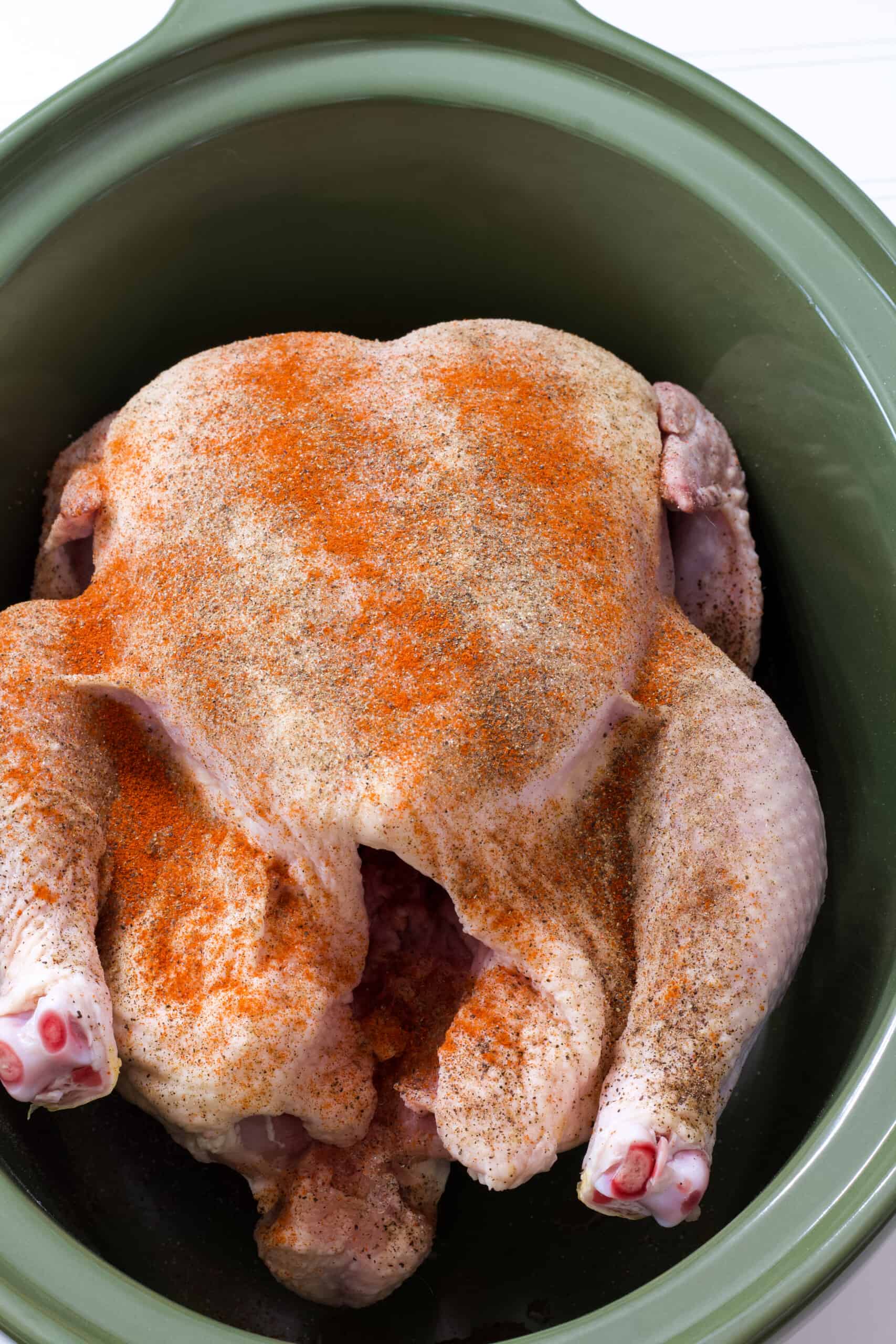 The raw seasoned chicken in the dark green crockpot.