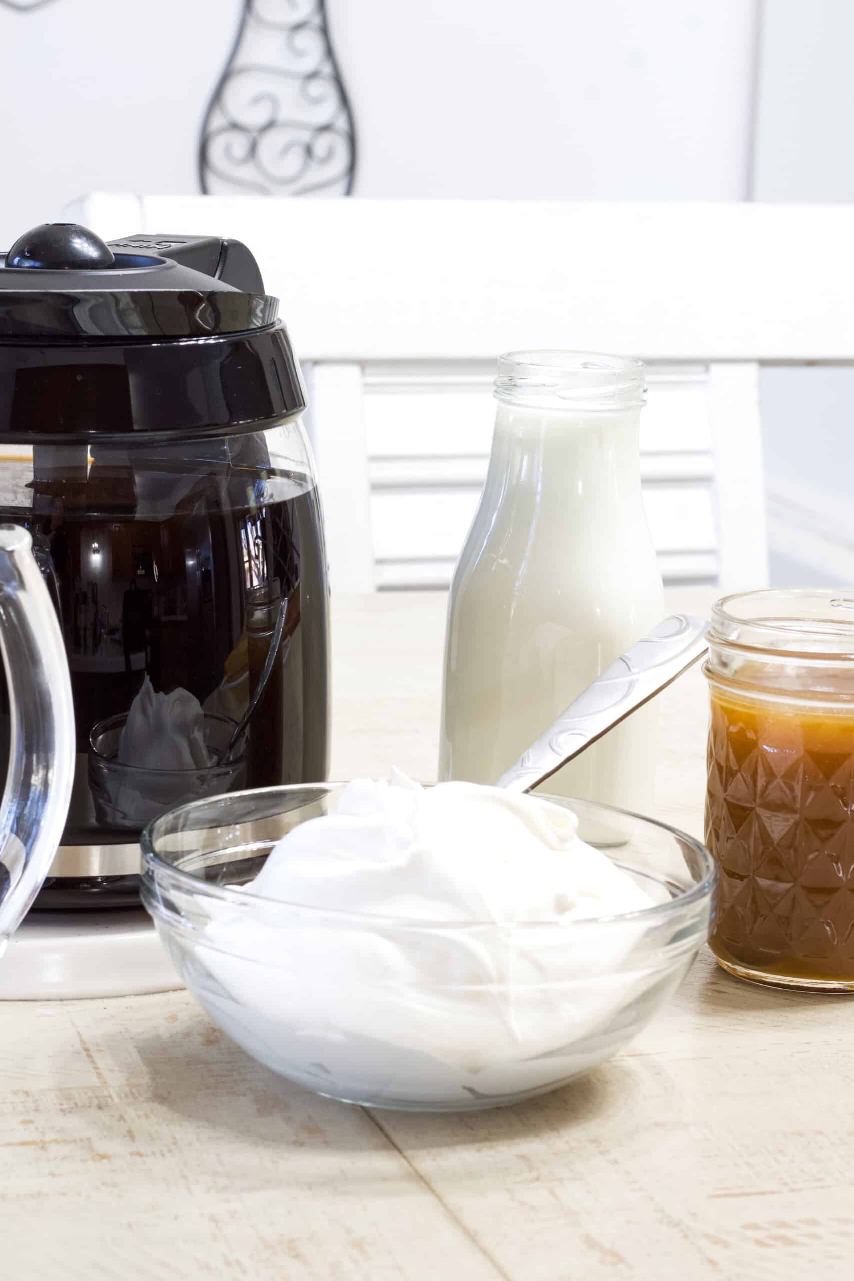 A pot of black coffee, a bottle of milk, a bowl of whipped cream and a jar of caramel sauce.