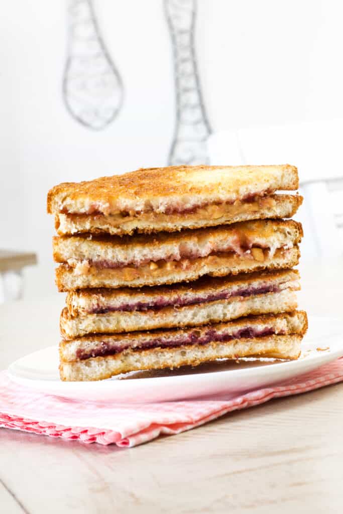 Two sandwiches cut in half stacked on top of each other, one with strawberry jelly and one with grape jelly.