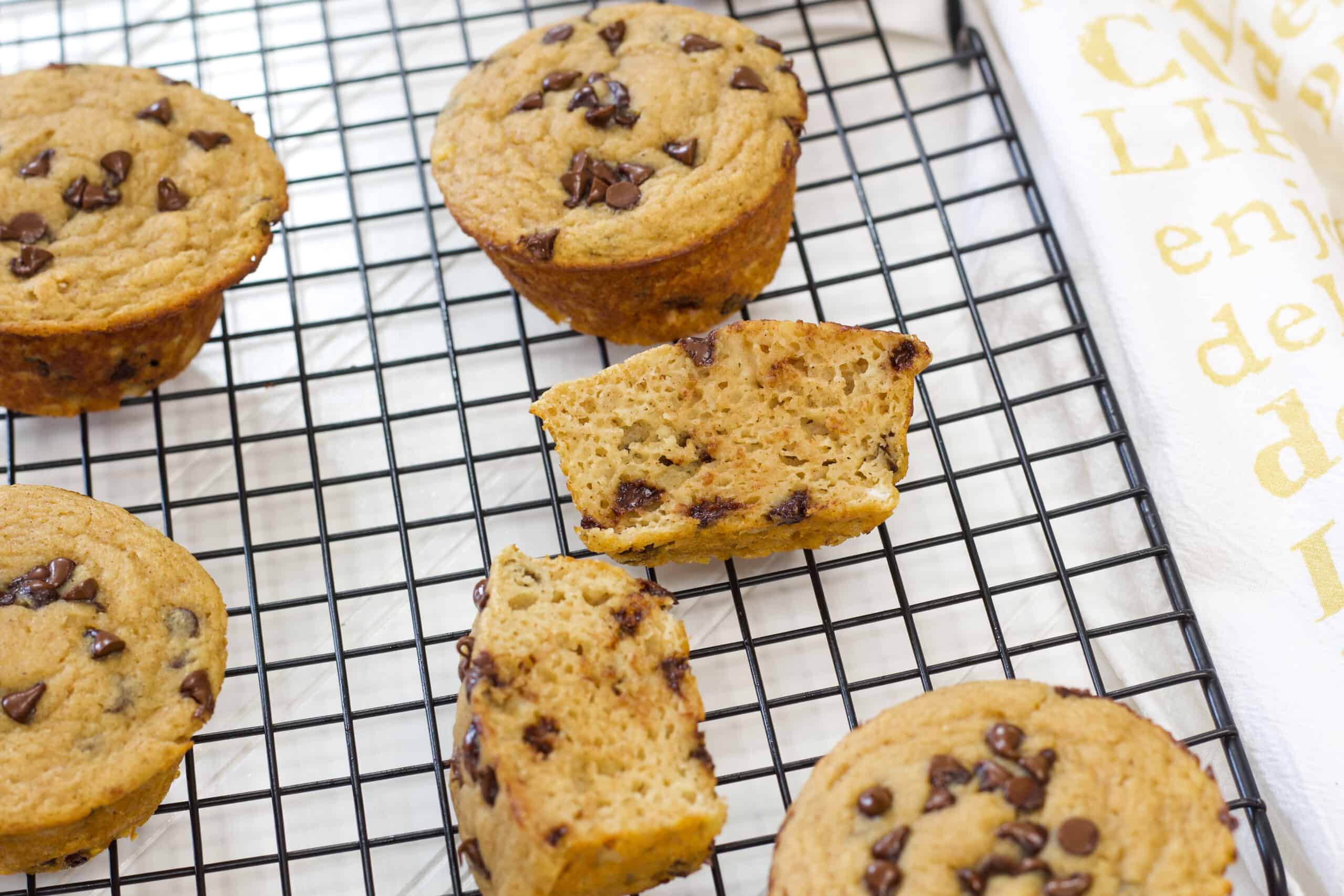 Several muffins on a black wire cooling rack and one muffin cut in half to show the inside.