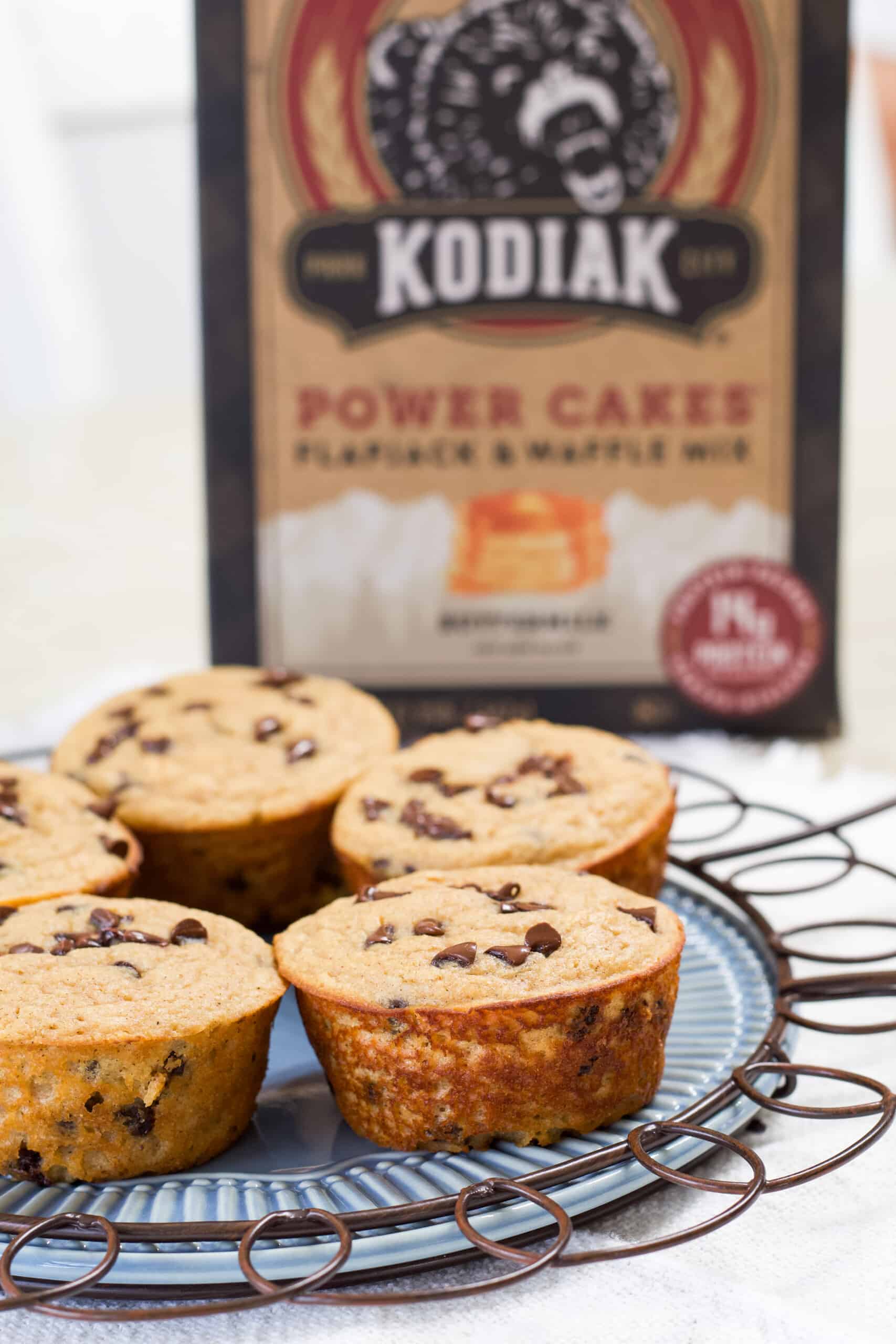 Five muffins on a light blue plate with the Kodiak Cakes box in the background.