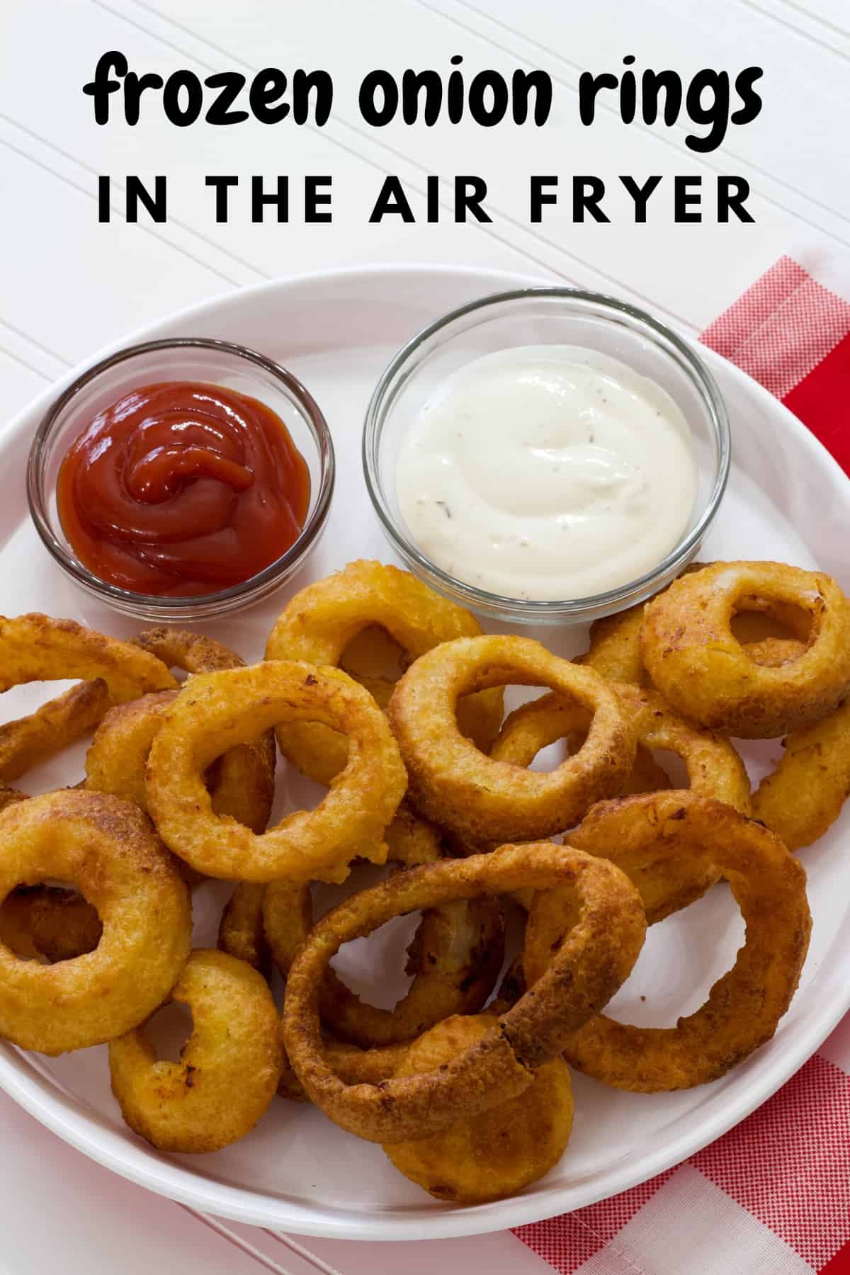 A white plate filled with onion rings and two small bowls of dipping sauces, ketchup and ranch dressing.