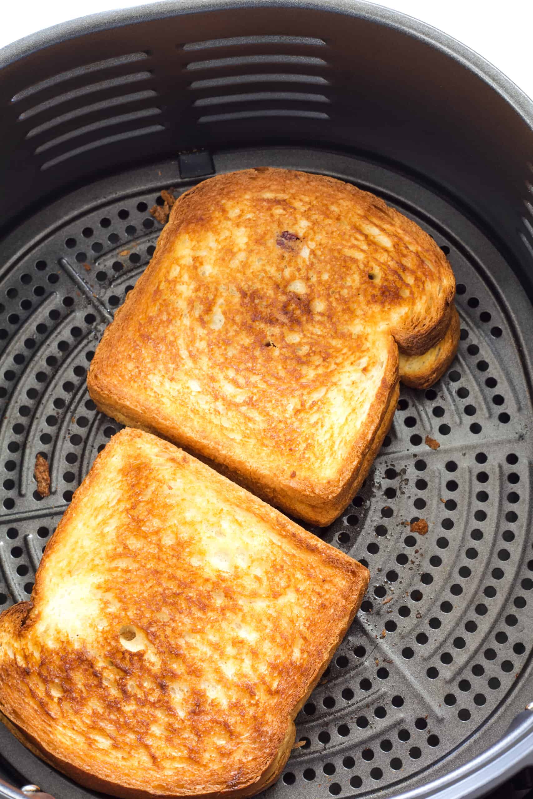 Two whole peanut butter and jelly sandwiches in the air fryer basket that have been air fried.