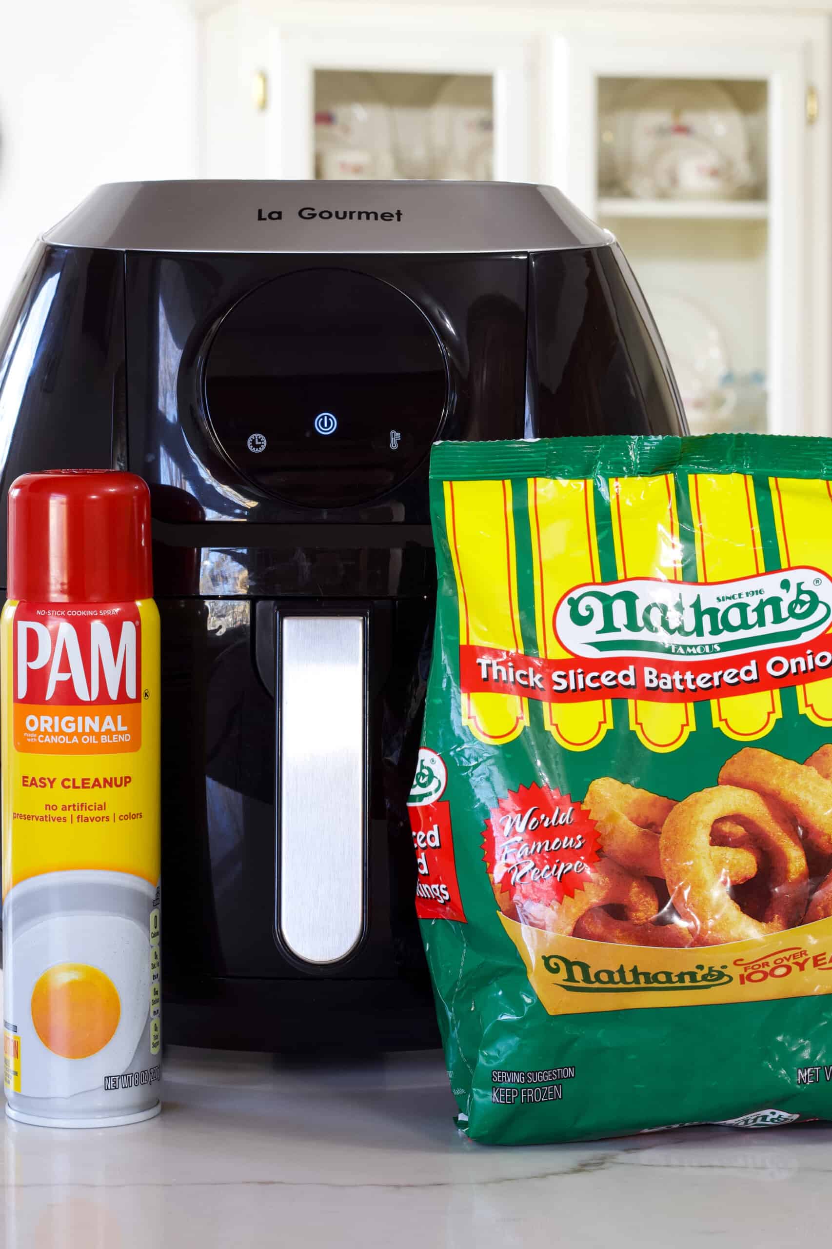 A can of Pam no-stick spray and a bag of Nathan's onion rings sitting on the counter in front of the air fryer.