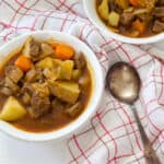 One bowl of soup and a silver soup spoon sitting on a white napkin that has red and brown plaid stripes on it.