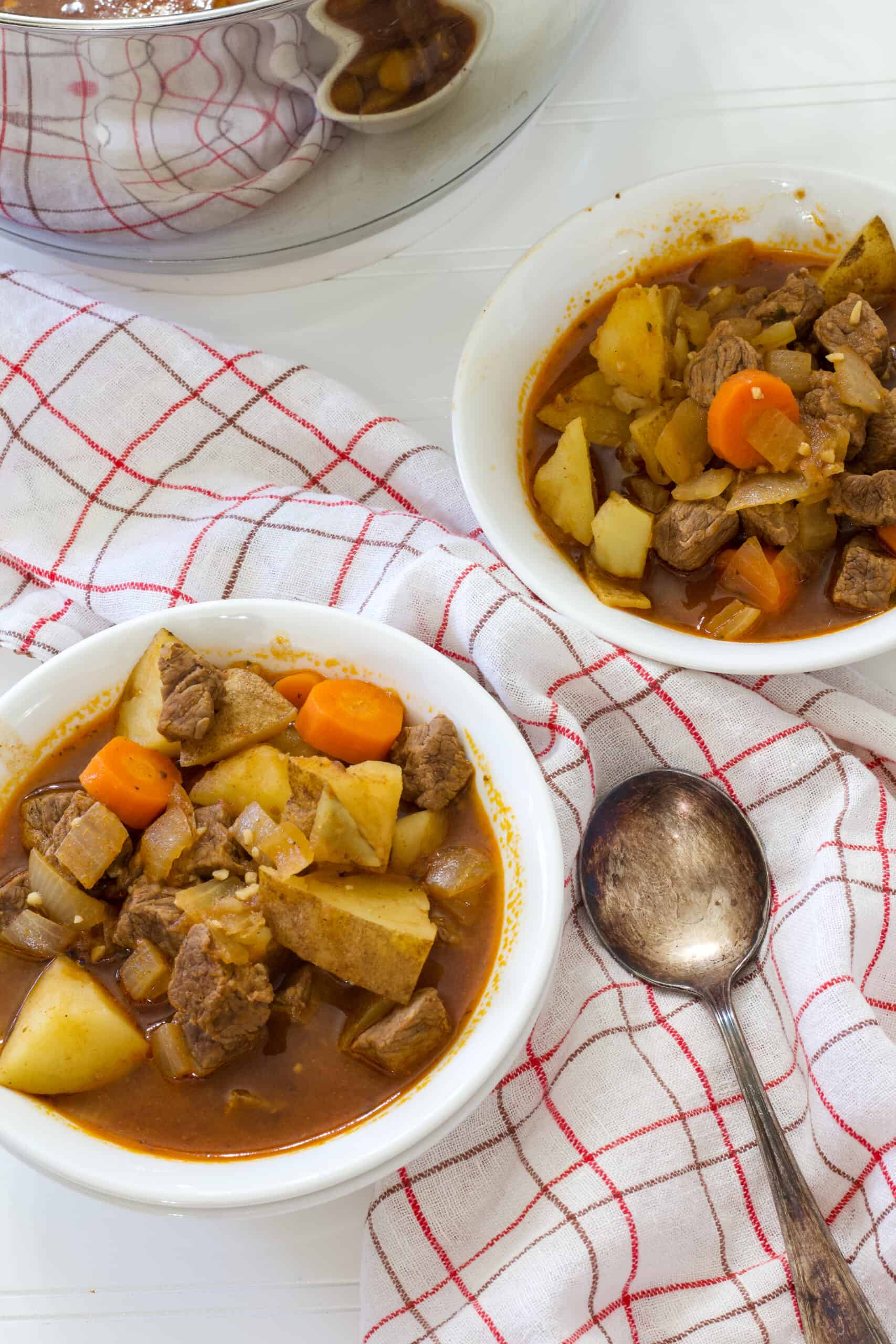 Two bowls of authentic german goulash soup with a silver soup spoon in between the bowls.