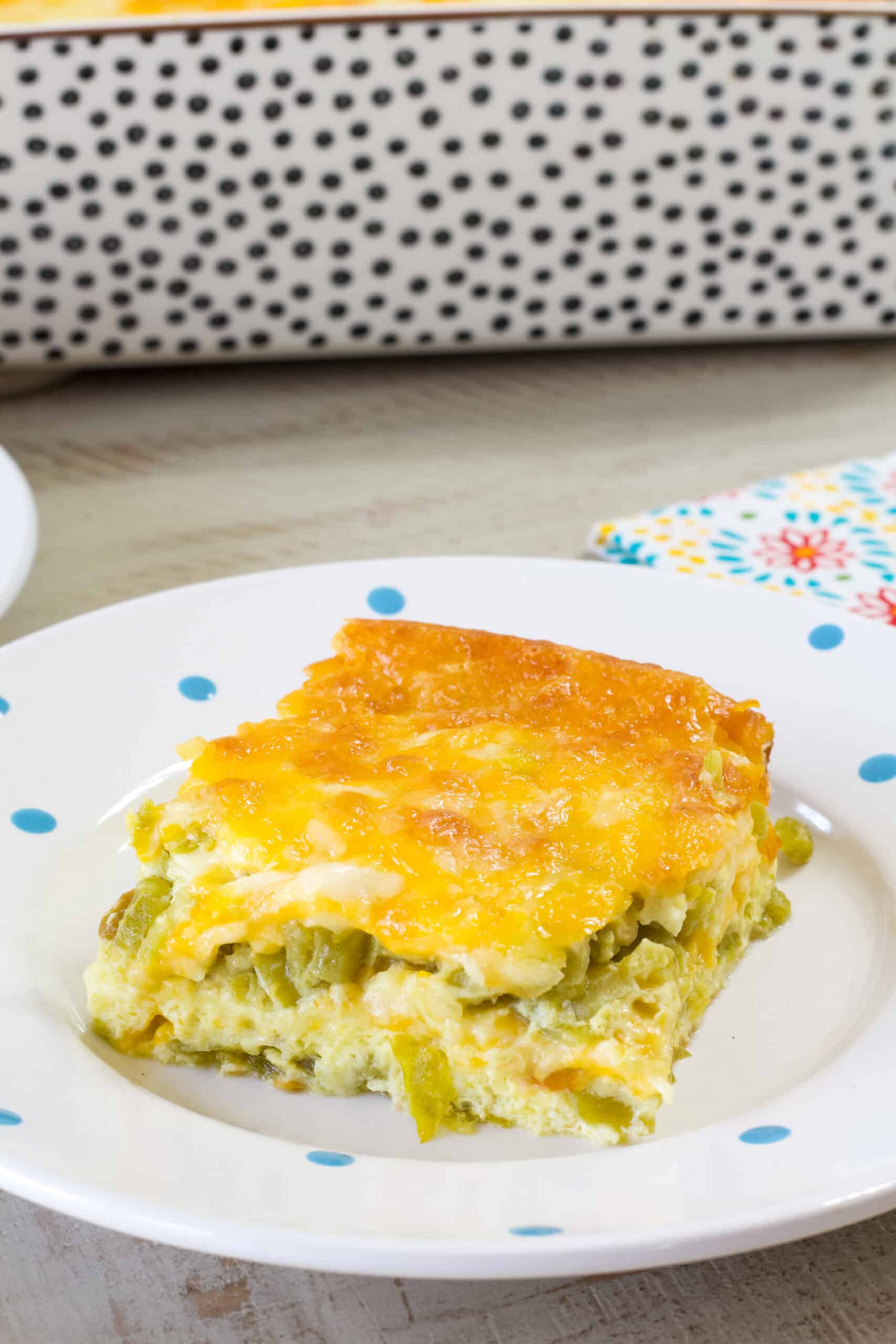 Close up side view of one serving of chile rellenos casserole on a white plate with blue dots.