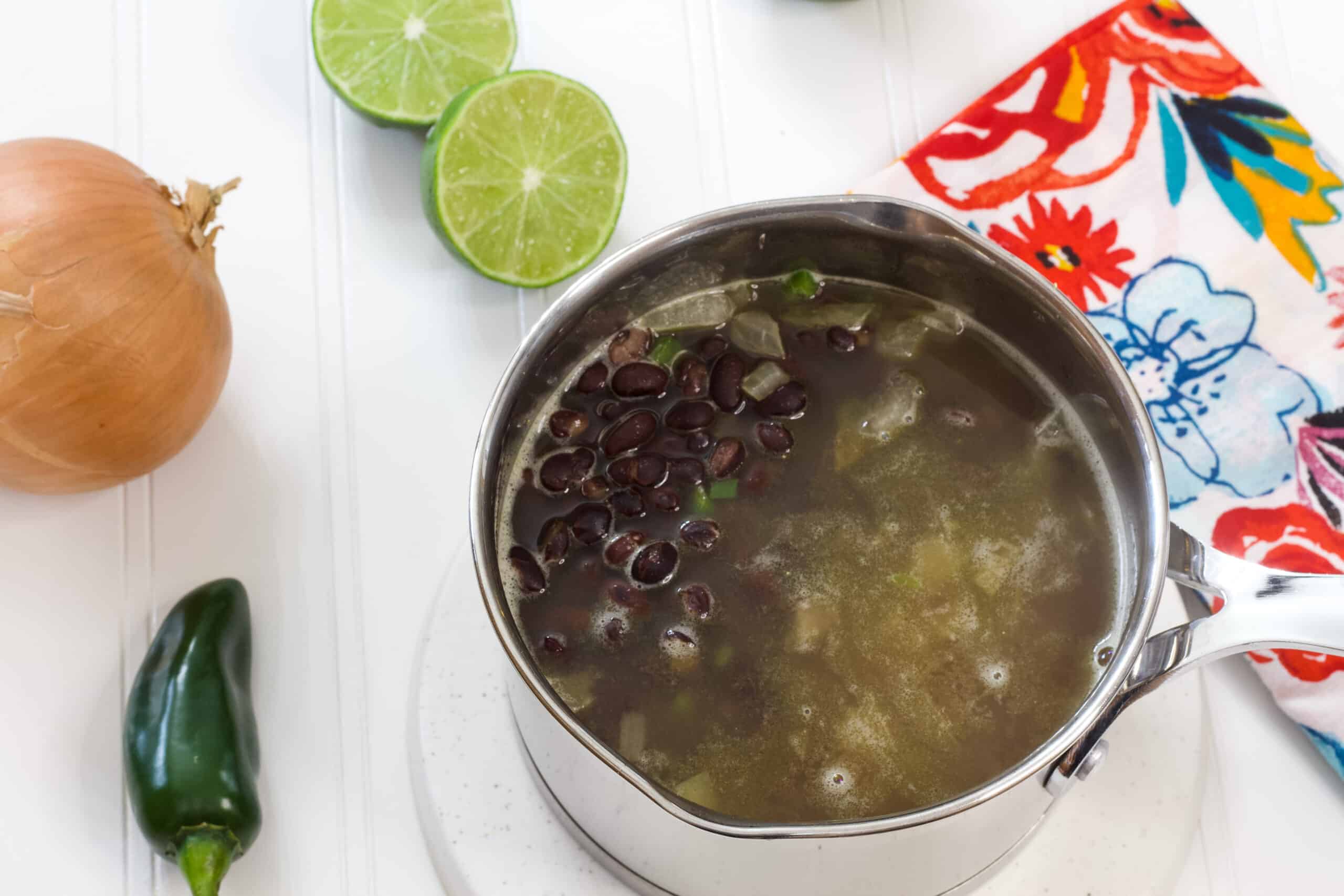 The pan of Mexican black beans with an onion, jalapeño and cut lime next to it.