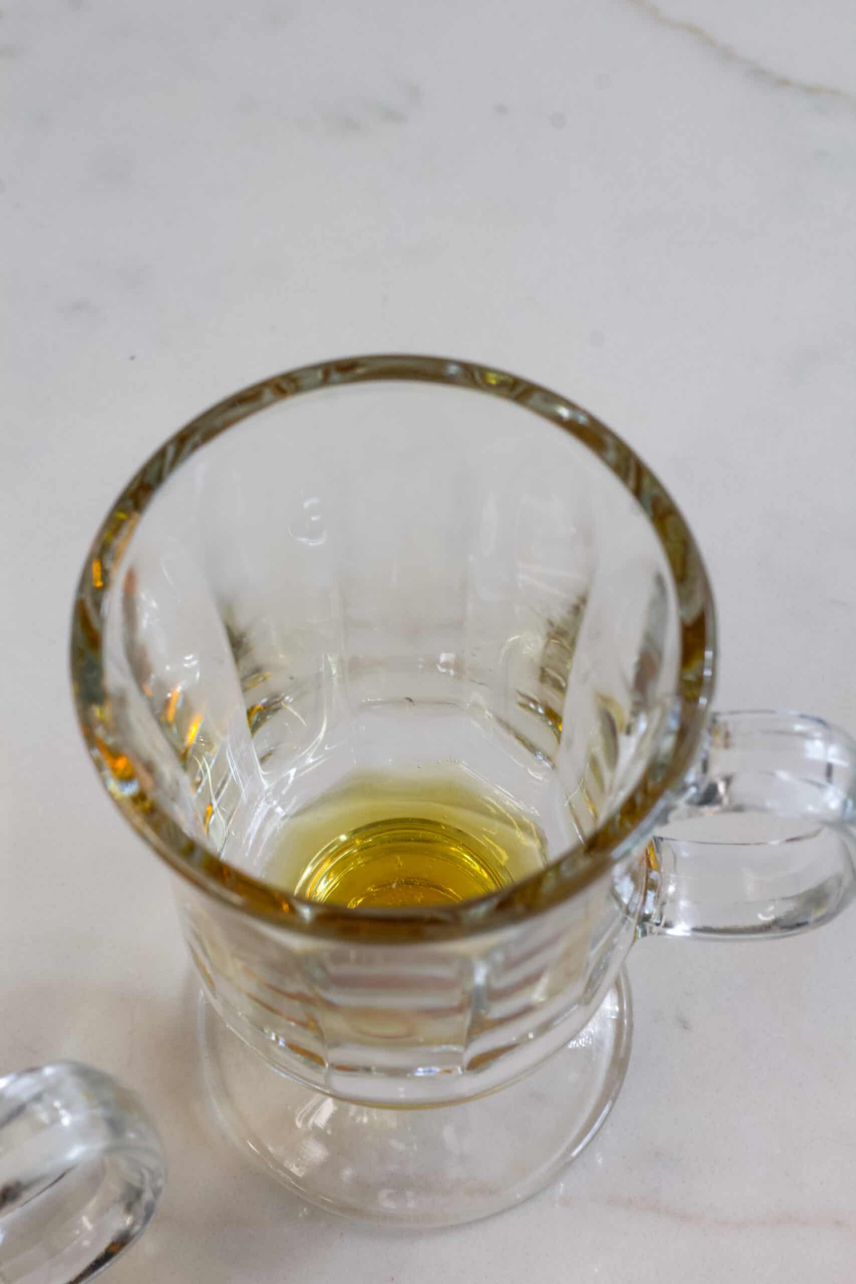 A clear glass coffee cup with a tablespoon of pure maple syrup in the bottom.