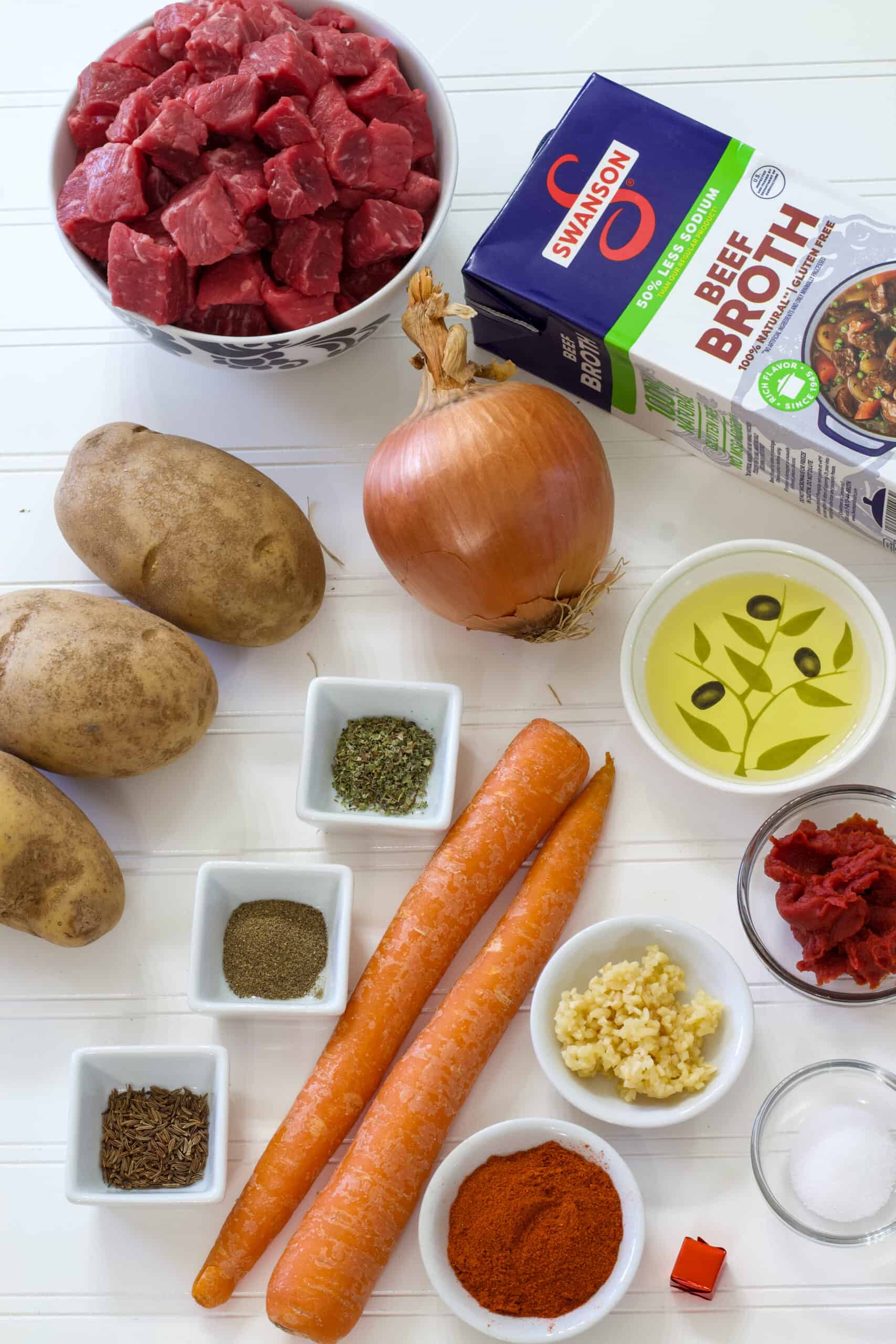All of the ingredients needed to make authentic german goulash soup laying on a solid white background.