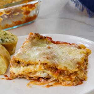 Close up of one serving of lasagna on a white plate.