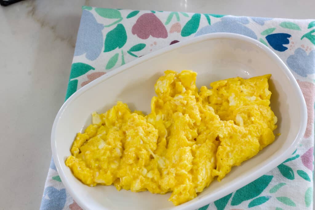 One serving of cheesy eggs on a white plate that is sitting on a floral napkin.