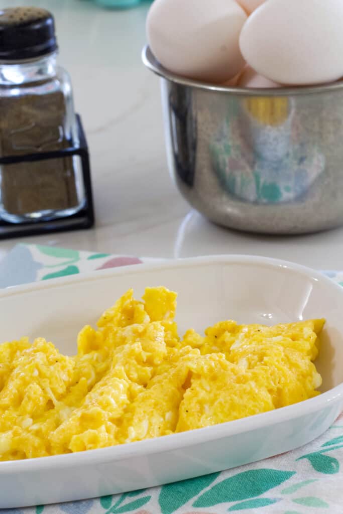 A serving of eggs in the foreground and a bowl of eggs and salt and pepper shakers in the background.