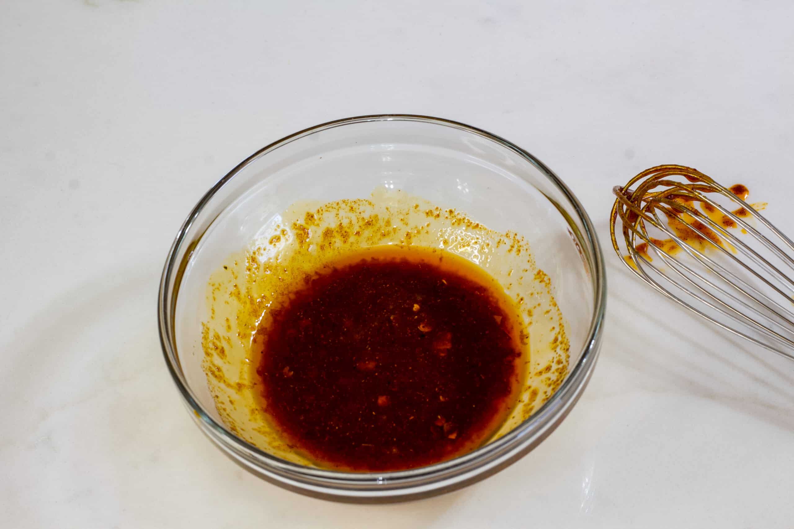 The spicy sauce in a small glass bowl with a whisk on the counter next to it.