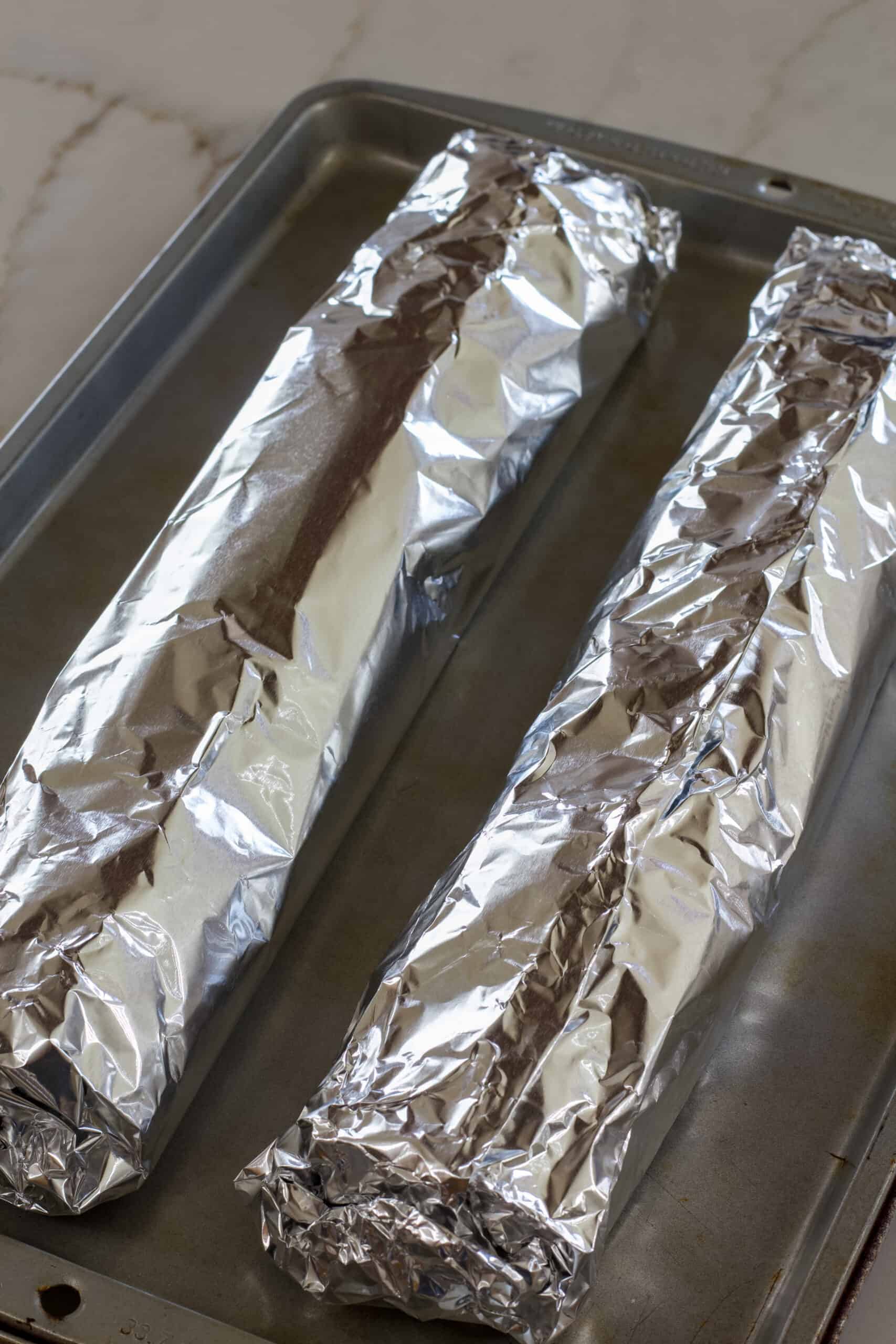 Both half loaves of garlic bread wrapped in aluminum foil ready to go into the oven.