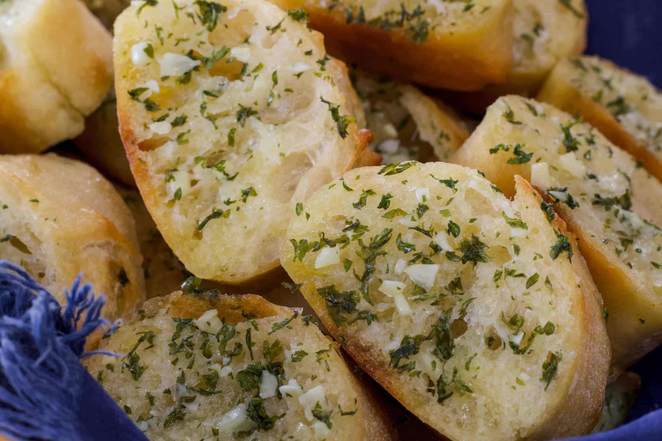 Close up view of slices of baguette garlic bread in a basket lined with a blue napkin.