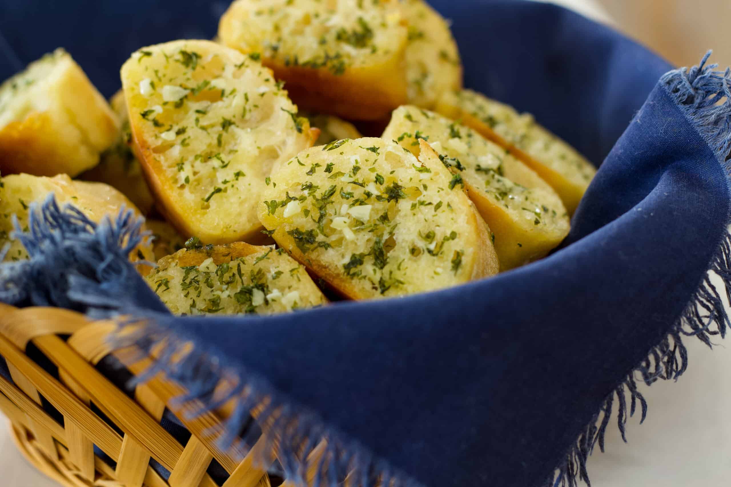 Side view of a basket lined with a dark blue napkin filled with slices of garlic bread.