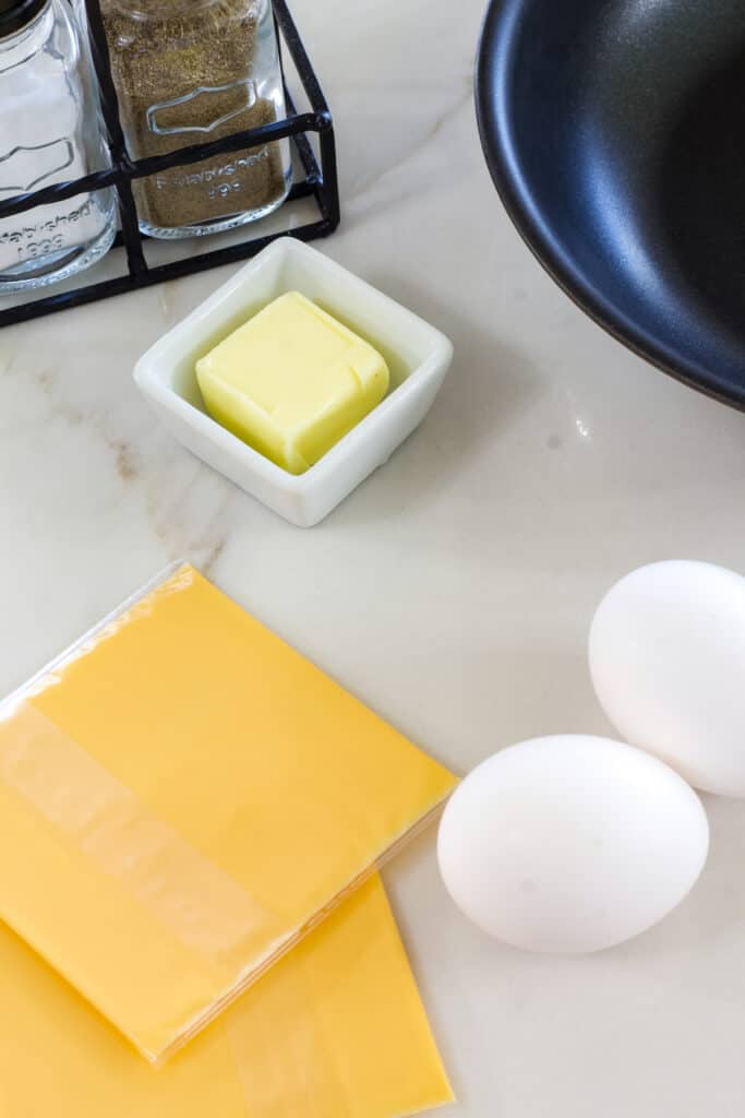 Two slices of cheese, two eggs, a tablespoon of butter, salt and pepper shakers and part of the small skillet used to cook the cheese eggs.